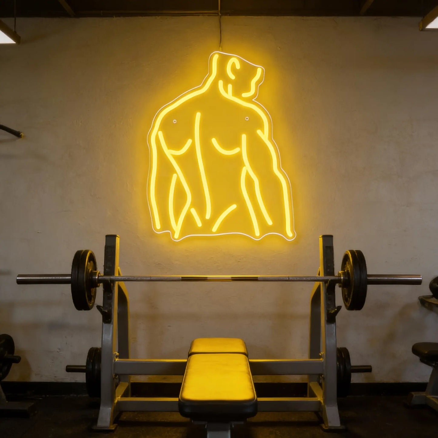 Neon sign of a muscular figure above a weight bench in a gym.